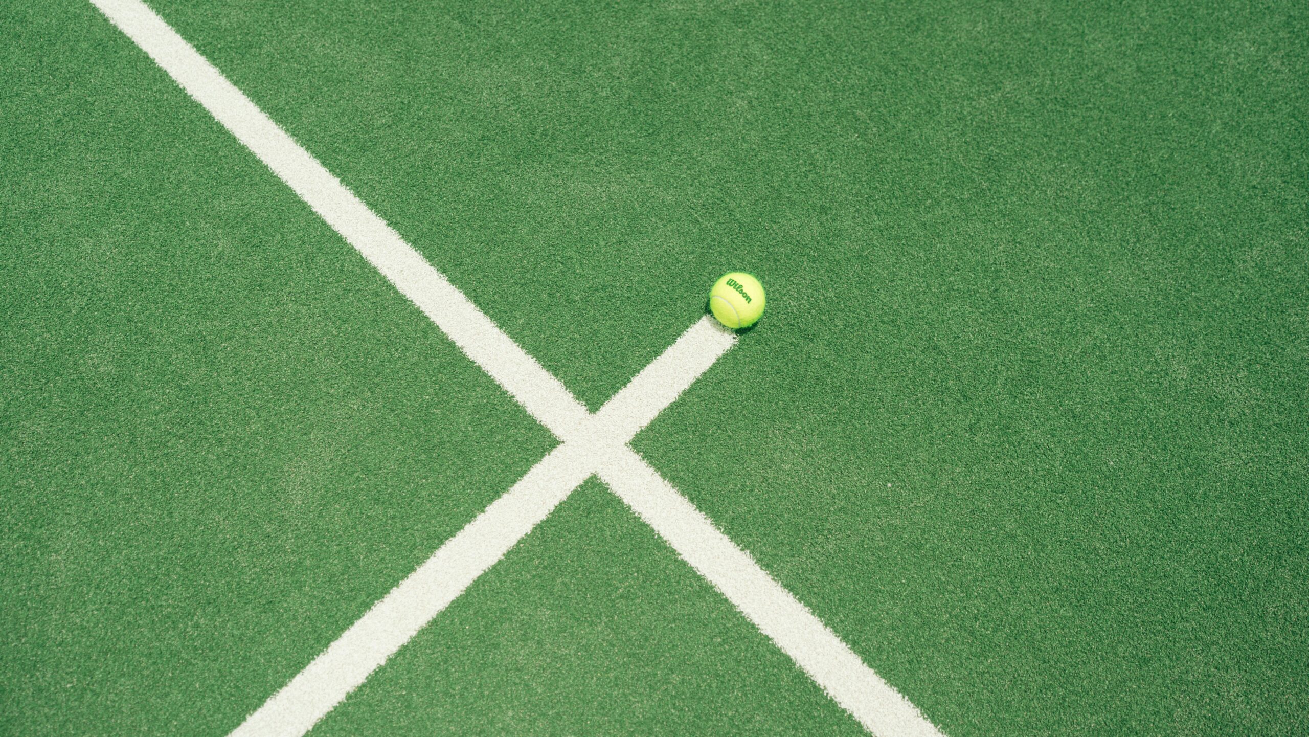 Tennis ball resting on an outdoor court — the grass, the precision, the colour that connects Wimbledon and Rolex