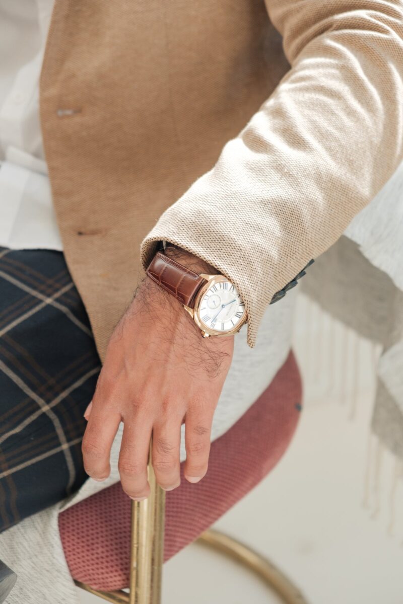 Gold-tone Cartier watch with a white Roman numeral dial and brown leather strap, worn with a beige jacket