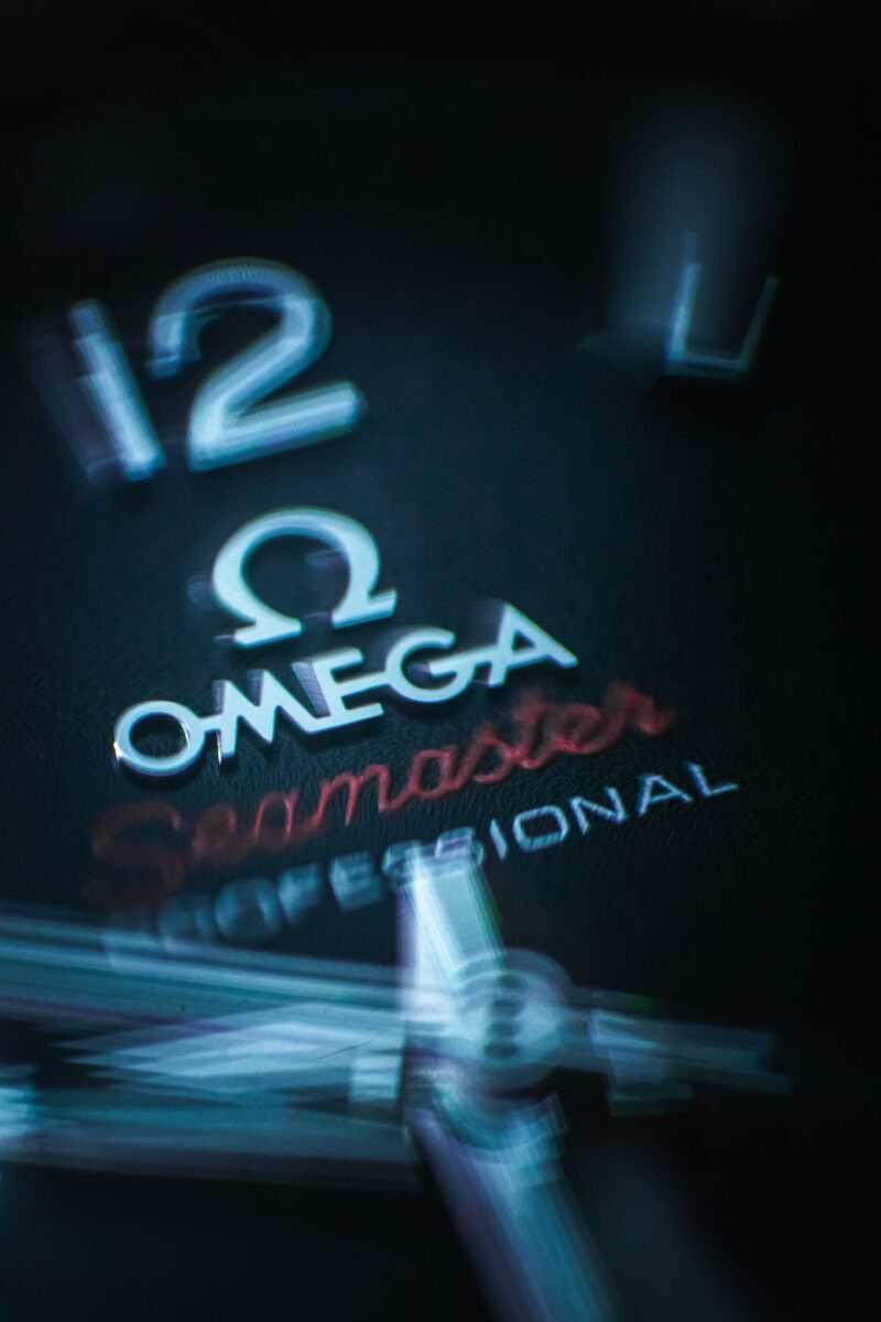 Macro detail of an Omega Seamaster dial showing the raised 12 numeral, Omega logo, red Seamaster lettering and watch hands.