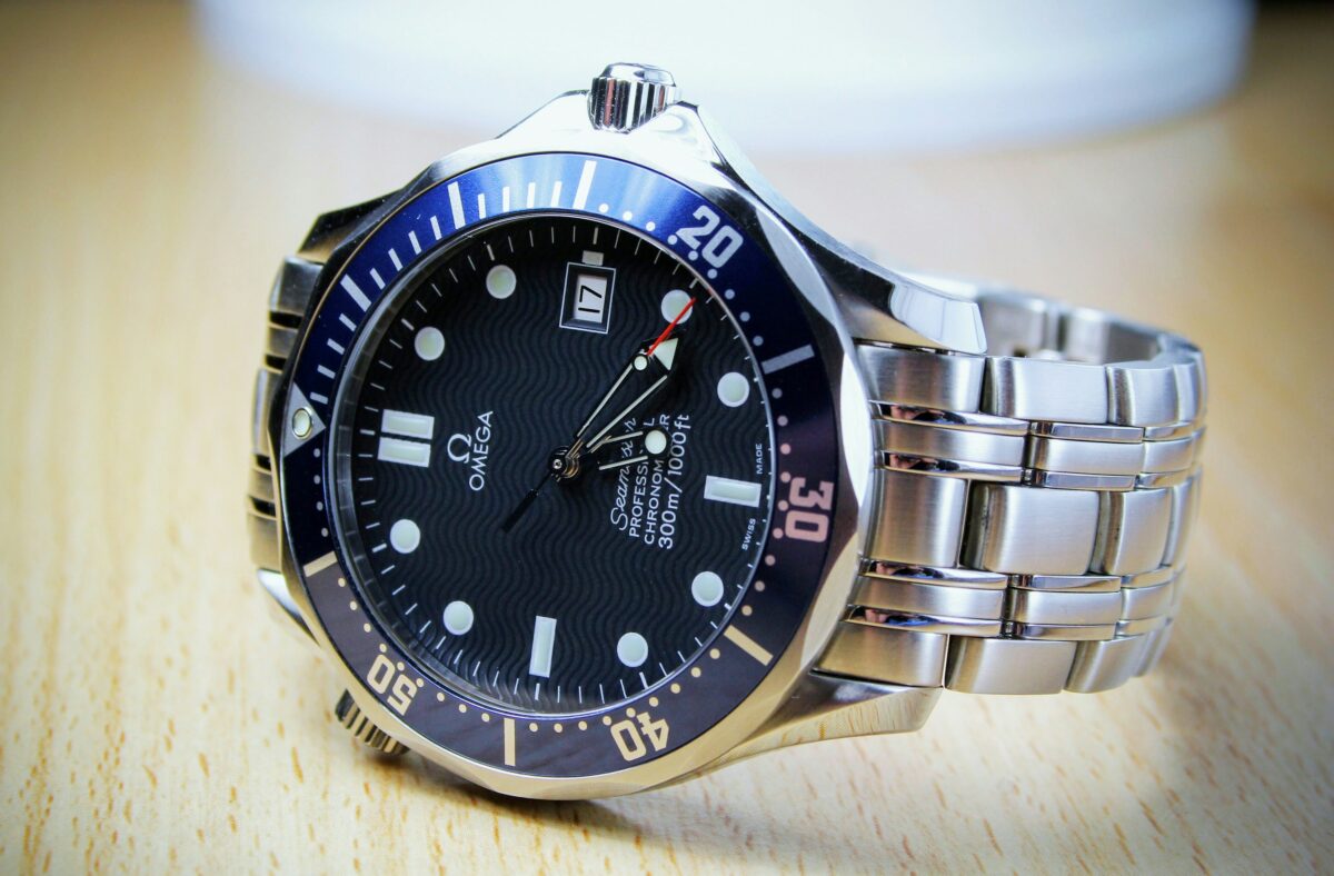 Omega Seamaster Professional with a blue wave-pattern dial, blue diving bezel and stainless steel bracelet on a wooden surface.
