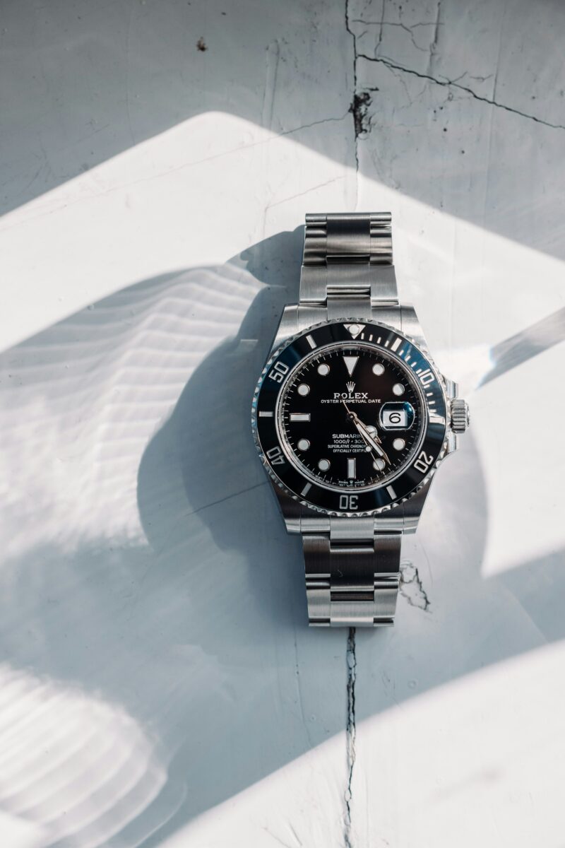 Rolex Submariner Date with a black dial and bezel and a stainless steel bracelet on a sunlit white surface.